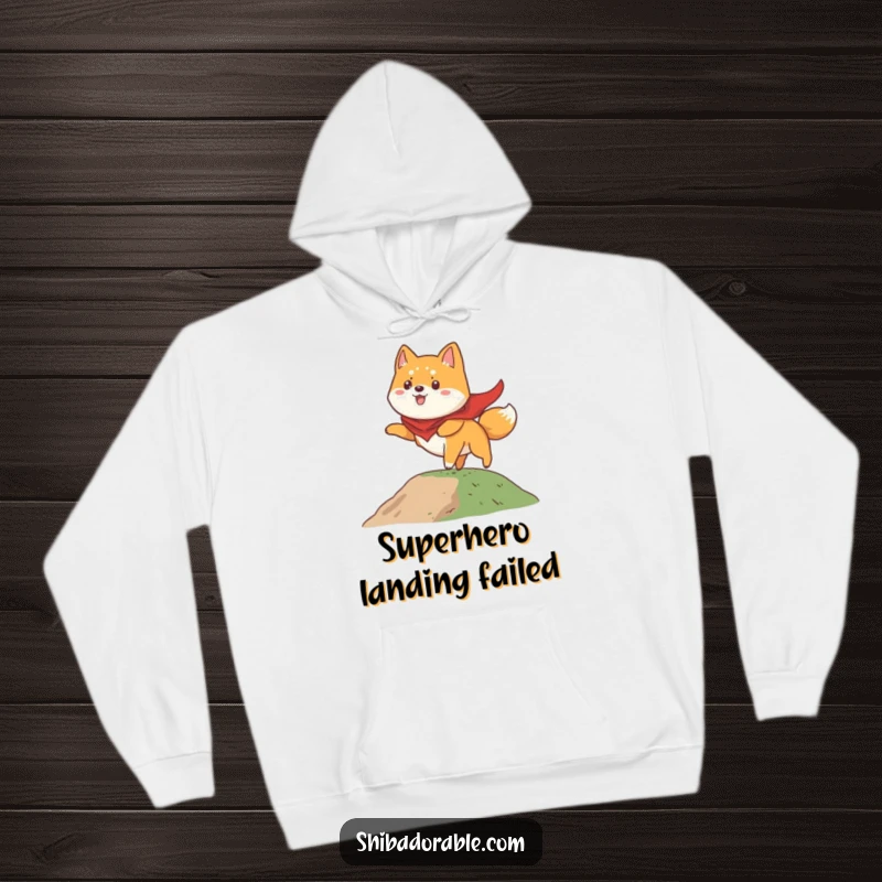 Funny Shiba Inu hoodie showcasing a dog in a cape, comically attempting to take flight from a small hill, full of heroic spirit.