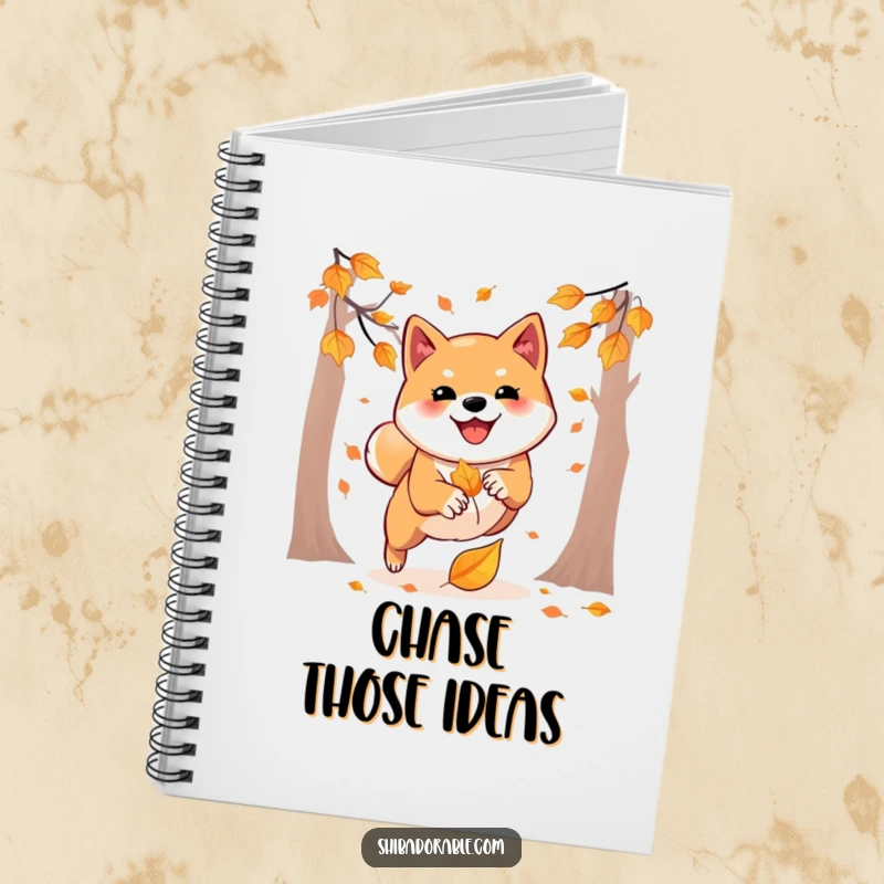 Funny notebook showcasing a Shiba Inu playfully pouncing on an autumn leaf, perfect for jotting down notes with seasonal flair.